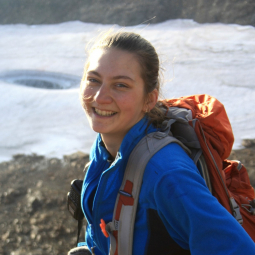 Grad student Anastasiia Mashkova wearing a backpack with a glacier in background