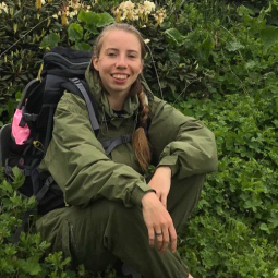 Grad student Irina Korsakova seated amongst green leafy plants in a forest.